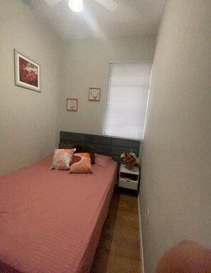 A bedroom with a bed, a nightstand, a window with blinds, and a ceiling fan. - Apto. Na Praia do Forte,😀cabo Frio - Centro (Centro Cabo Frio)