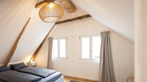 Une chambre avec un plafond en pente, un lit avec une literie grise, un tapis à motifs et un luminaire suspendu.