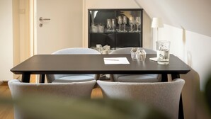 Un coin repas avec une table dressée pour deux personnes, un buffet contenant de la verrerie et une lampe.