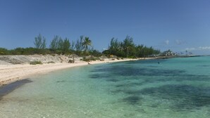 Een strand met helder turquoise water, wit zand en schaarse begroeiing.