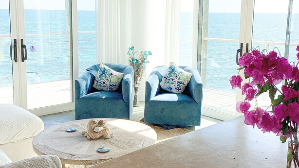 Een kamer met twee blauwe fauteuils, een kleine ronde tafel en uitzicht op zee door grote glazen deuren.