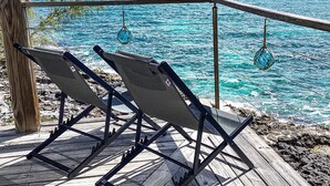 Een houten terras met drie loungestoelen gericht op een turquoise zee.