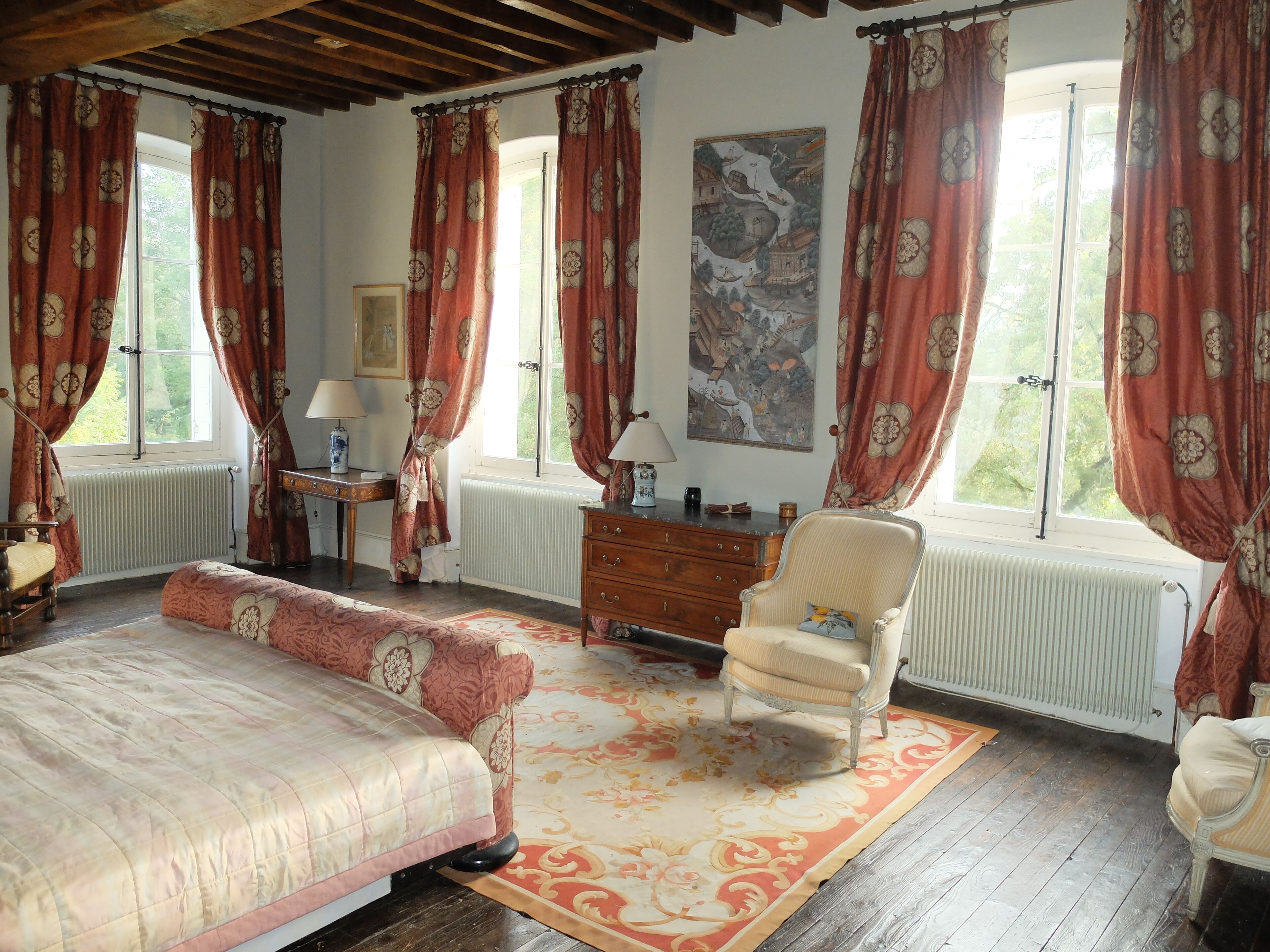 A bedroom with a bed, a chair, a dresser, and a window with curtains.