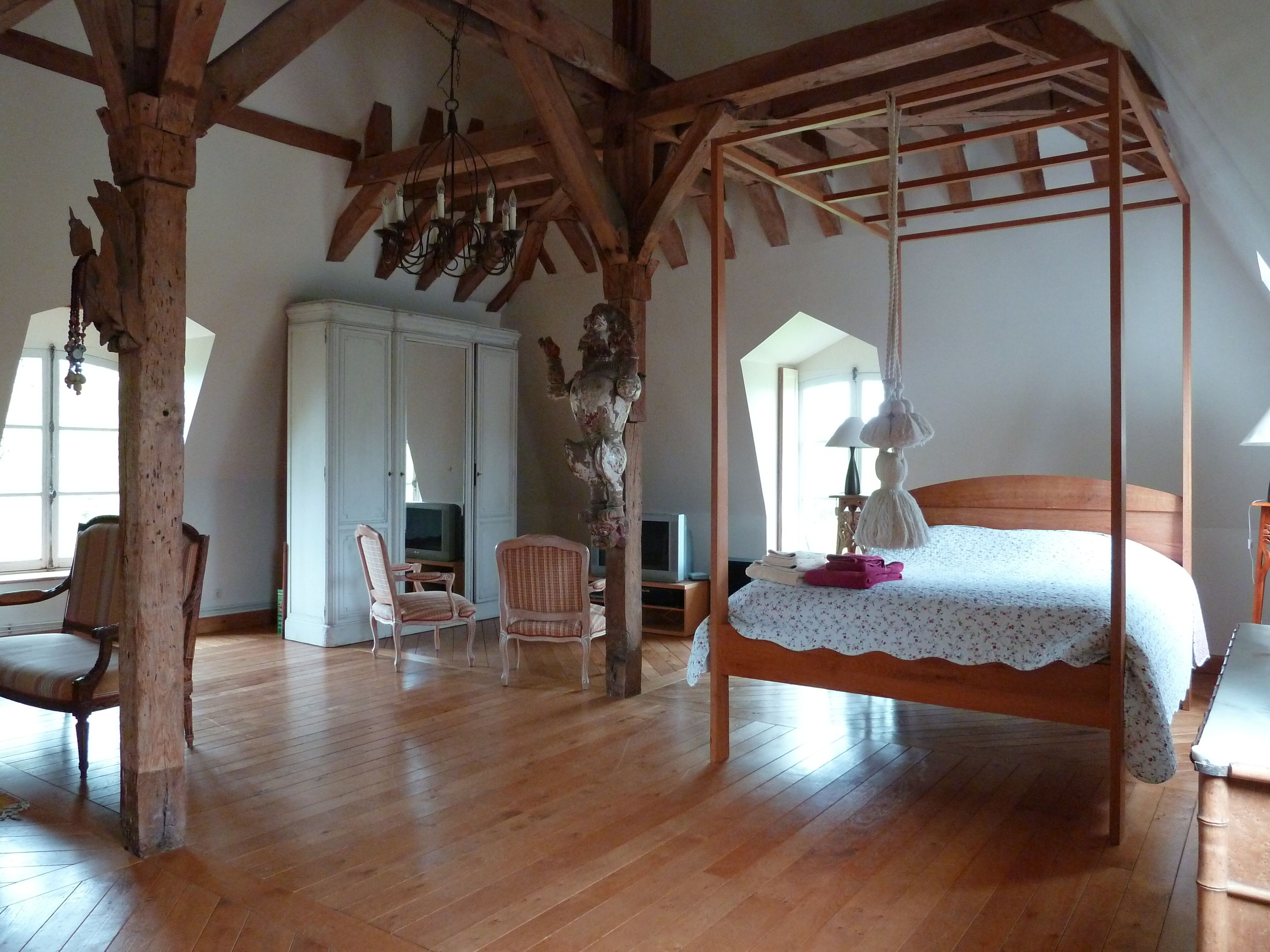 A spacious room with a wooden floor, a four-poster bed, a large wardrobe, and a television.