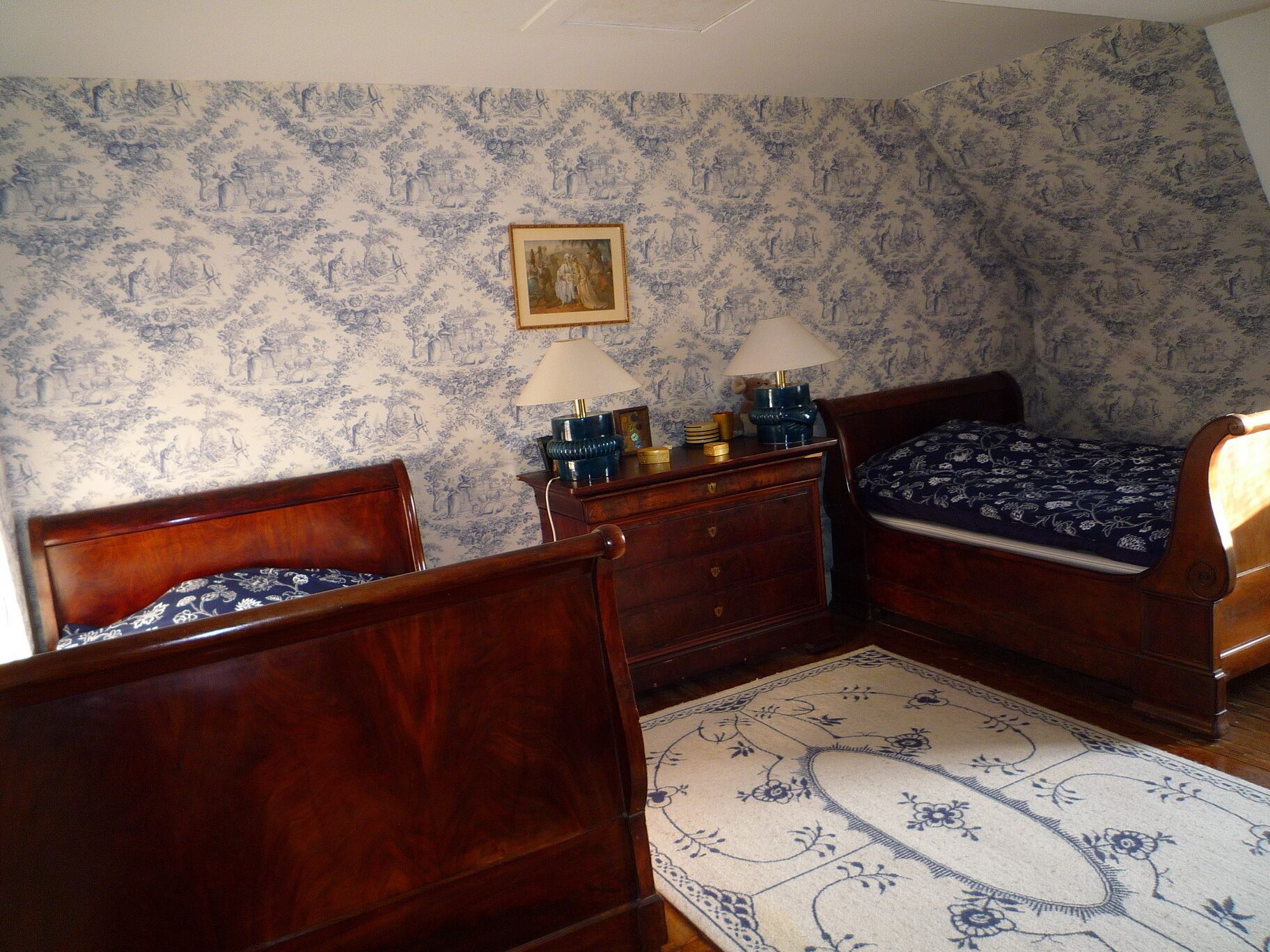 A bedroom with two wooden beds, a dresser, a lamp, and a patterned rug.