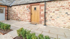 A stone building with a wooden door, a small sign, and a paved entrance area with plants.