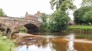 A stone bridge over a calm river with greenery on both sides.