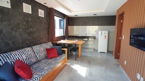 A modern living area with a sofa, a dining table, and a kitchen in the background. - Casa Janaína (Camaçari)