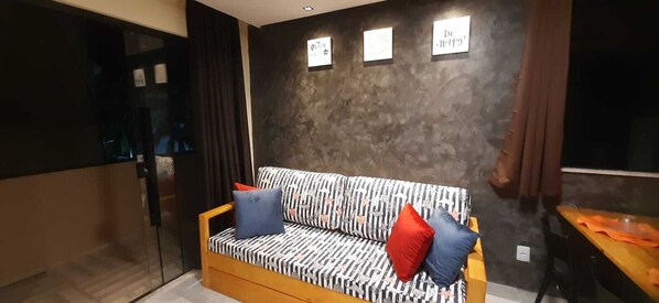A modern living room with a patterned sofa, a wooden coffee table, and a dark textured wall with three framed signs.