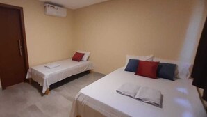 A room with two beds, a door, and a wall-mounted air conditioner. - Casa Janaína (Camaçari)