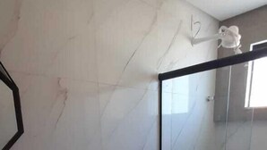 A modern bathroom with a marble wall, a wooden vanity with a sink, a toilet, and a glass shower enclosure. - Casa Janaína (Camaçari)