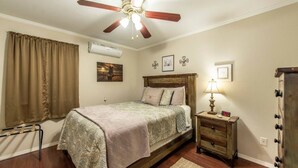 Un dormitorio con cama, mesita de noche, lámpara, ventilador de techo y aire acondicionado de pared.