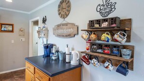 Una cocina con mostrador de madera, un adorno de pared con temática de café, un reloj y estantes con tazas y utensilios de cocina.