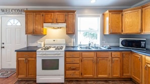 Una cocina con armarios de madera, estufa, microondas y pileta.