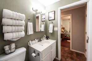 A bathroom with a white sink, toilet, and towel rack. There is a mirror above the sink and a door leading to another room. - Songbird Haven Cozy Country Getaway (Waco)