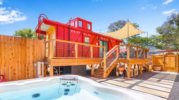 A red building labeled "Rock Island" with a wooden deck, a hot tub, and a covered area with a canopy. - Chic Caboose in Wimberley Square (Wimberley)