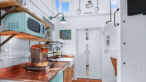 A compact kitchen with a vintage microwave, coffee machine, and wooden cabinets. - Chic Caboose in Wimberley Square (Wimberley)