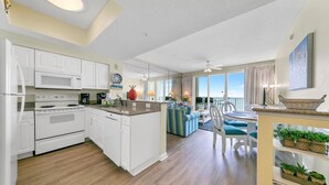 A modern kitchen with white cabinets, a central island, and a dining area with a view. - Majestic Sun 0908B - Incredible Gulf and pool views, steps to the beach! (Miramar Beach)