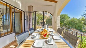 A sunlit outdoor dining area with a wooden table set for two, surrounded by metal railings and large windows.