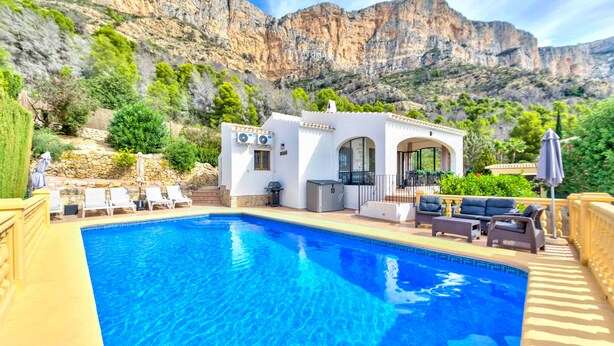 A swimming pool with lounge chairs and a patio area, set against a mountainous backdrop.