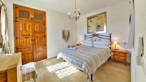 A bedroom with a bed, bedside tables, a chandelier, a wardrobe, and a painting on the wall.