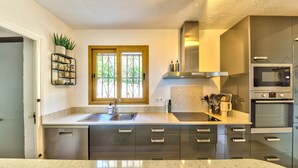A modern kitchen with a built-in oven, stainless steel appliances, and a window with a view of greenery.
