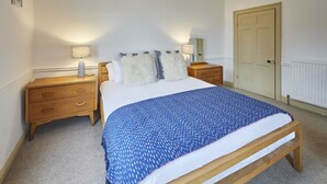 Une chambre à coucher avec un lit, deux tables de chevet, une commode, une porte et un radiateur.