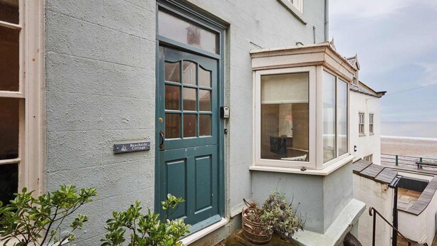 Une petite maison avec une porte verte, une baie vitrée et une enseigne indiquant son nom.