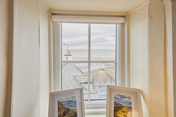 Ein Fenster mit Blick auf eine Küstenlandschaft, darunter ein Leuchtturm und ein Strand.