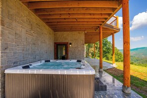 A hot tub under a wooden pergola with stone walls, overlooking a scenic landscape.