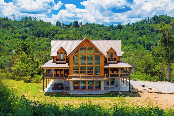 A large wooden cabin with multiple balconies, situated in a forested area with a clear view of the surrounding landscape.