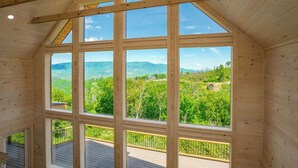 Ein Holzinnenraum mit großen Fenstern, die einen Blick auf eine grüne Landschaft und ferne Hügel ermöglichen.