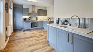 Een moderne keuken met grijze kastjes, een roestvrijstalen spoelbak en een houten vloer.
