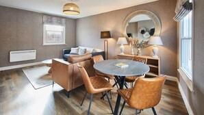 Een moderne woonkamer met een ronde eettafel, lederen fauteuils, een bank en een grote spiegel.