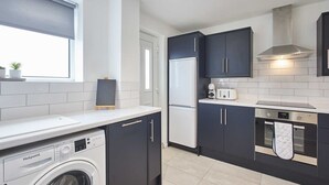 Une cuisine compacte avec des meubles de rangement sombres, un lave-linge encastré, un réfrigérateur et un four.