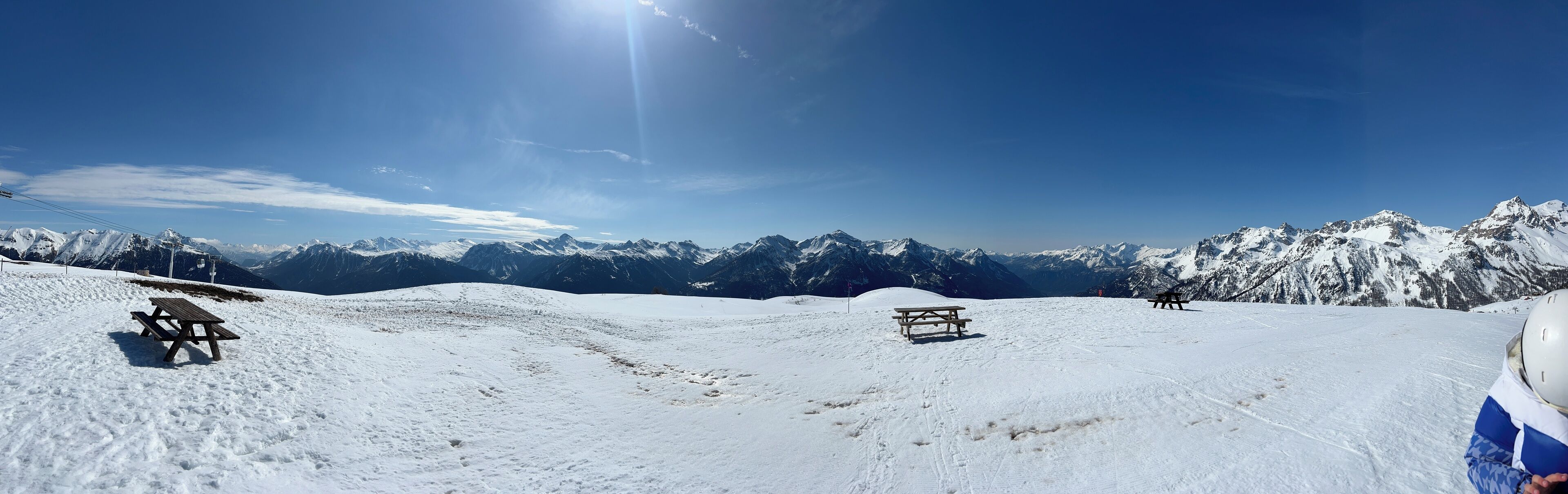 Un paysage de montagne enneigé, avec des tables de pique-nique et un télésiège en arrière-plan.