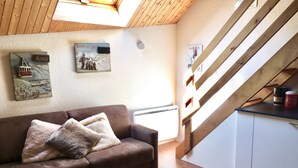 Una sala de estar acogedora con un sofá marrón, techo de madera y una escalera.
