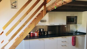 Una cocina con armarios blancos, una escalera de madera y un microondas de acero inoxidable.