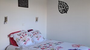 Ein ordentlich bezogenes Bett mit floralem Bettbezug, eine Wandleuchte und eine dekorative Blattschablone.