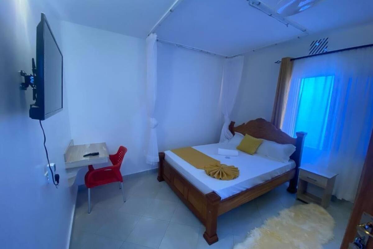A bedroom with a bed, a desk, a chair, and a TV mounted on the wall.