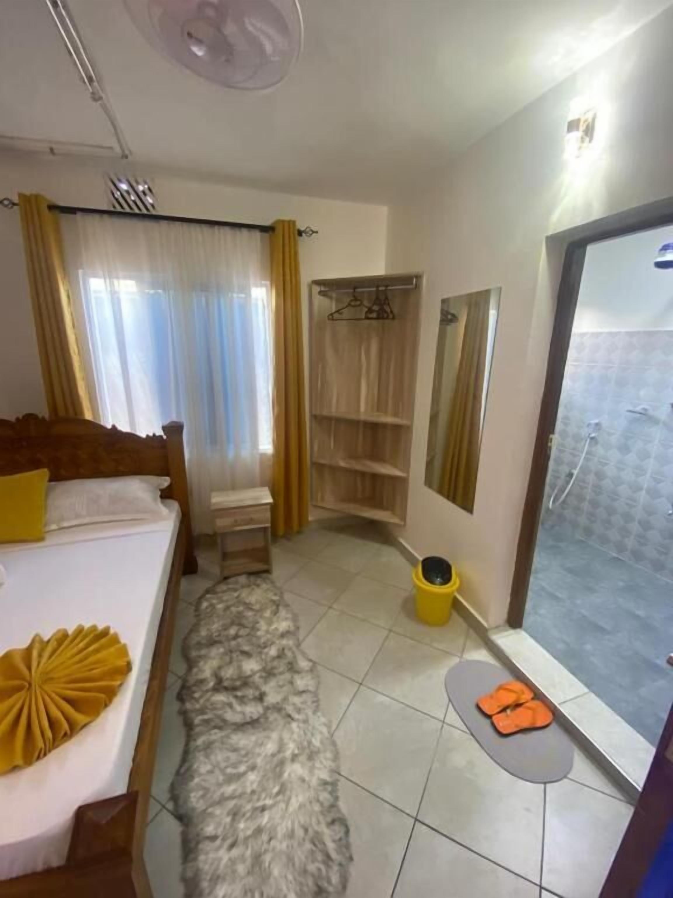 A hotel room with a bed, a small table, a shower area, and a bathroom with a toilet.