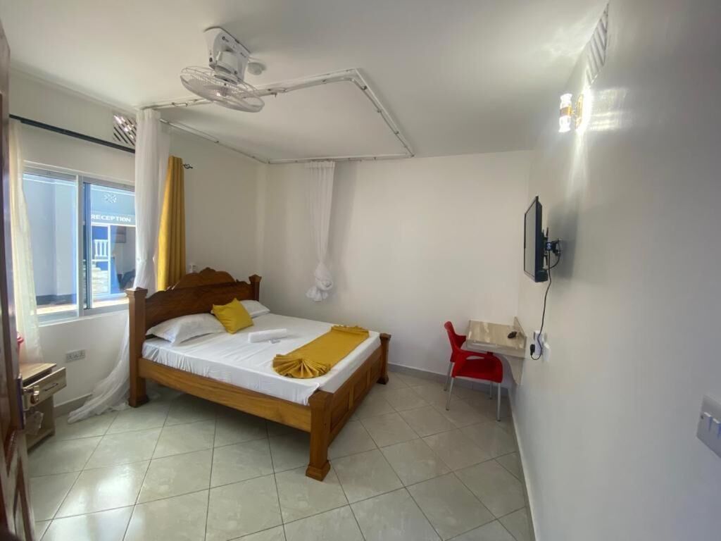 A bedroom with a wooden bed, a ceiling fan, a red chair, and a TV mounted on the wall.