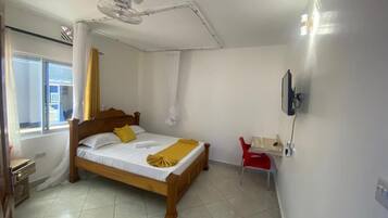 A bedroom with a wooden bed, a ceiling fan, a red chair, and a TV mounted on the wall.