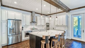 A modern kitchen with white cabinets, a stainless steel refrigerator, a large island with stools, and hanging pendant lights. - Naturewalk NEXT to Pool! LSV/Golf Cart & Bikes! 4 Kings! Pet Friendly! (Santa Rosa Beach)