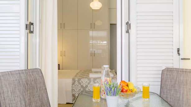 A glass table with two glasses of orange juice, a fruit bowl, and a vase with flowers. - Casa Tsipa (Corfu)
