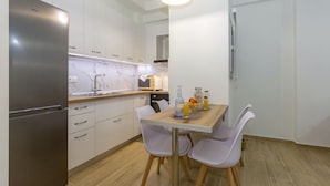 A modern kitchen with white cabinets, a stainless steel refrigerator, and a dining table with chairs. - Casa Tsipa (Corfu)