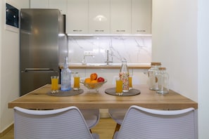A modern kitchen with a stainless steel refrigerator, marble backsplash, and a wooden dining table with chairs. - Casa Tsipa (Corfu)