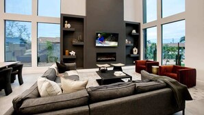 A modern living room with a large gray sectional sofa, a flat-screen TV mounted on the wall, and a fireplace. - Scottsdale Retreat - Pool, Outdoor Grill, Firepit (Scottsdale)