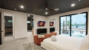 A modern bedroom with a large bed, a ceiling fan, a view of the outside, and a bathroom visible through an open door. - Scottsdale Retreat - Pool, Outdoor Grill, Firepit (Scottsdale)
