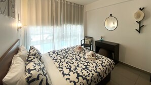 Ein Hotelzimmer mit einem Bett, einem Sessel, einem Schreibtisch, einem Spiegel und einem Wandhaken für Hüte.